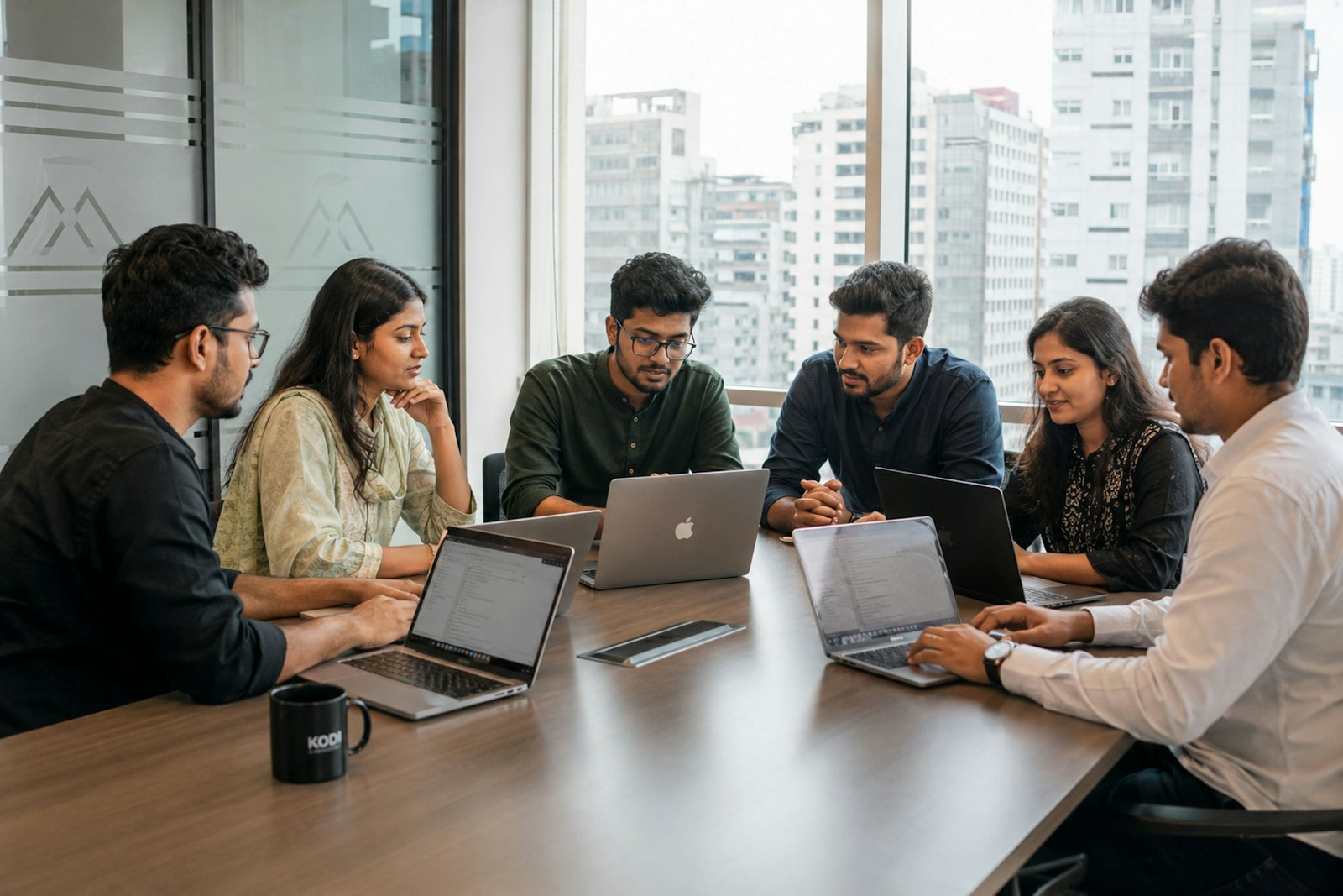 A team around a boardroom table with laptops, city skyline behind them